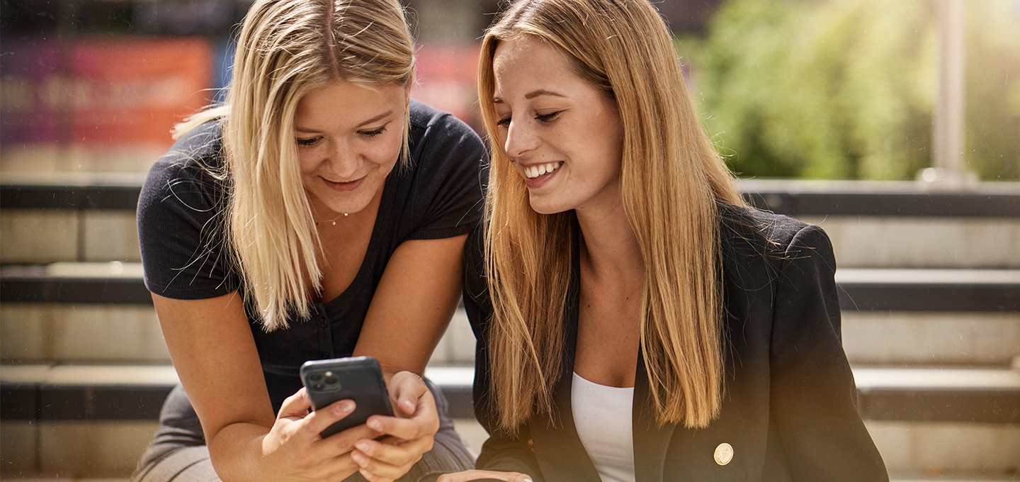 Zwei Studentinnen blicken auf ein Smartphone.