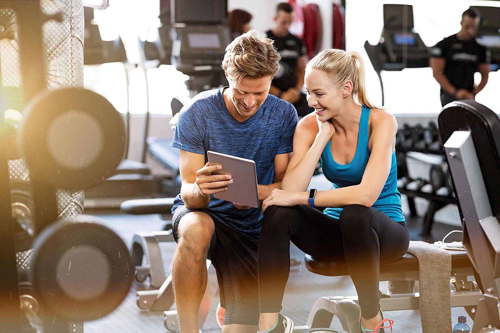 Mann und Frau im Fitnessstudio gucken auf Tablet